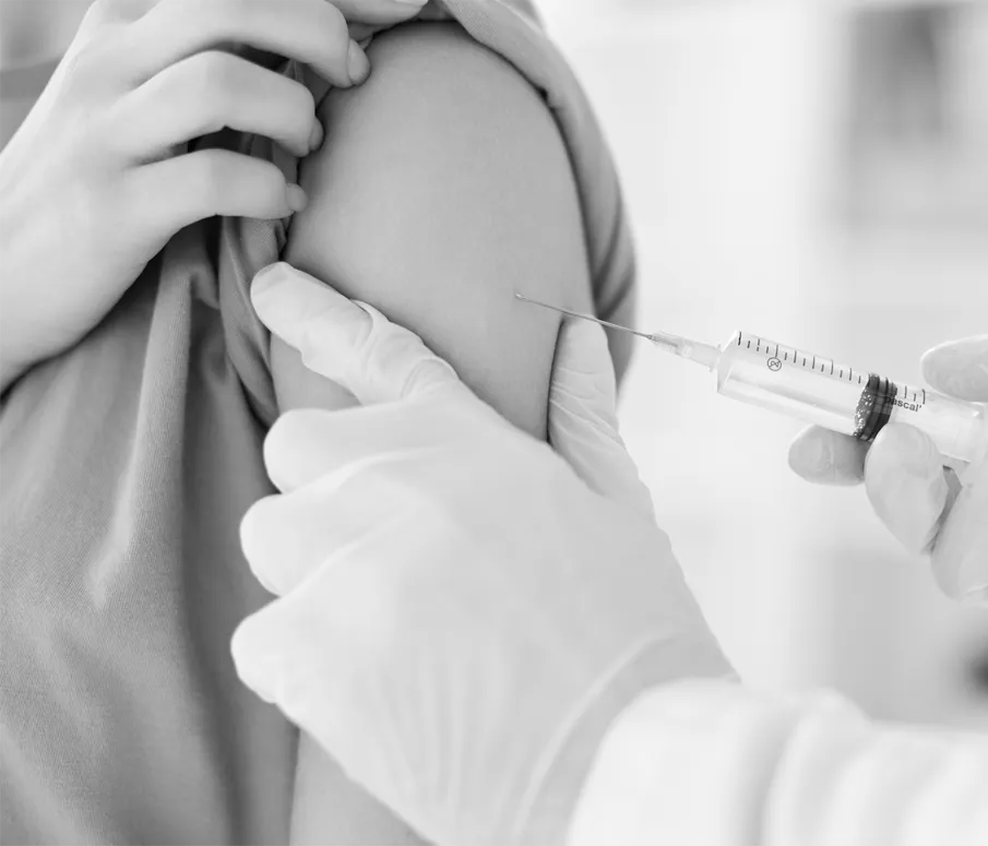 A person receiving an injection in the upper arm from a healthcare professional wearing gloves, using a syringe.